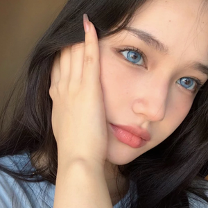 Close-up of a person with blue eyes and dark hair, wearing a light blue top.