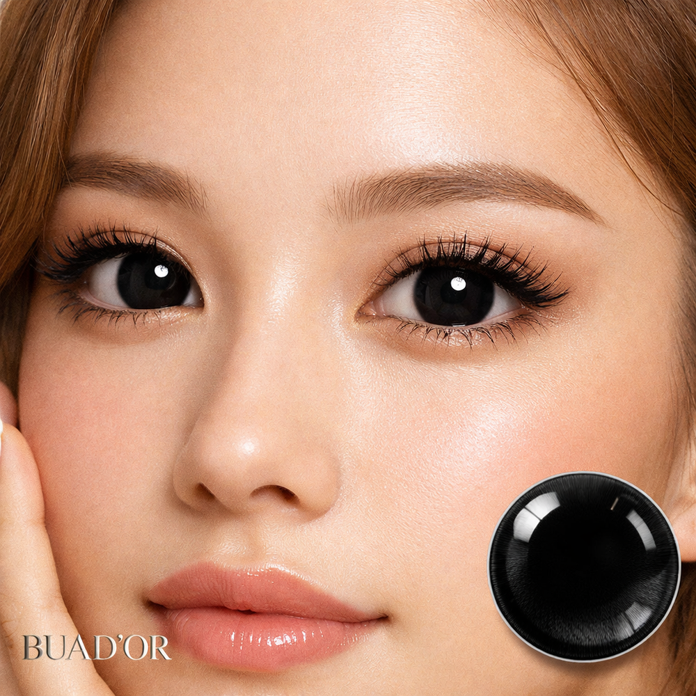 Close-up of a woman's face with a black contact lens displayed next to her eye, featuring the brand 'BUAD'OR'.