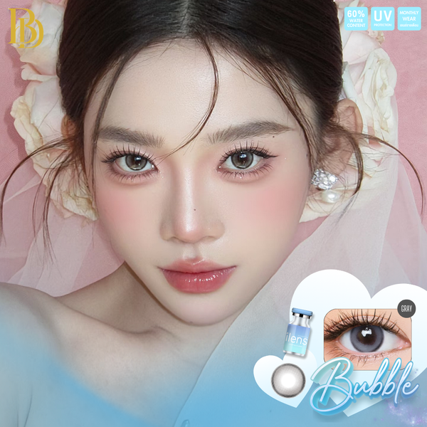 Close-up beauty shot of a woman wearing contact lenses, with pink floral background and contact lens packaging/graphics in the lower right corner. The product appears to be Bubble Gray colored contact lenses, shown on the model and in a small product inset.
