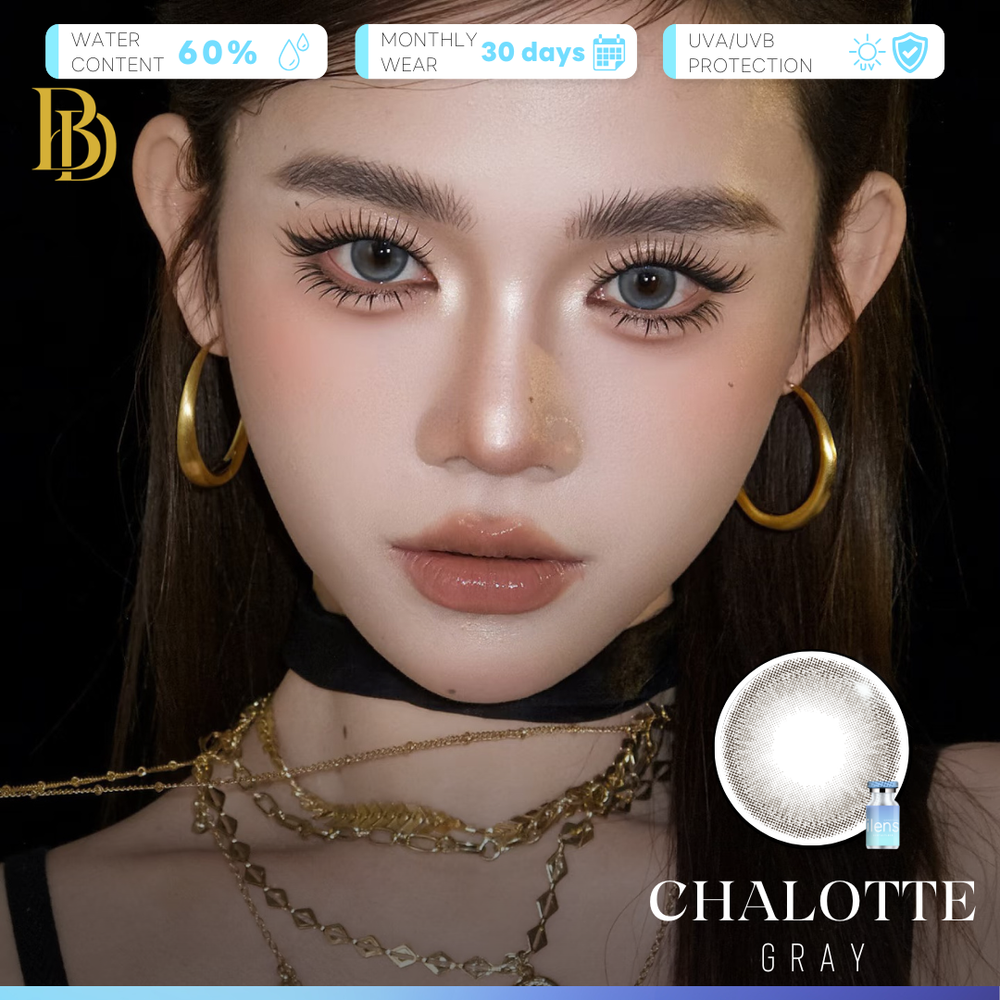 A close-up of a model wearing gray contact lenses, with gold hoop earrings and layered gold necklaces against a black background. The image includes text overlays highlighting product features such as water content, monthly wear, UV protection, and the color name 'CHALOTTE GRAY' alongside a circular lens graphic.