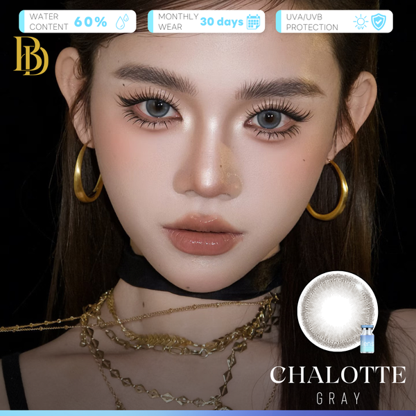 A close-up of a model wearing gray contact lenses, with gold hoop earrings and layered gold necklaces against a black background. The image includes text overlays highlighting product features such as water content, monthly wear, UV protection, and the color name 'CHALOTTE GRAY' alongside a circular lens graphic.