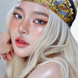 Woman with blonde hair and a colorful headscarf posing against a neutral background