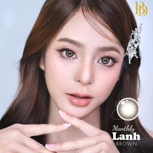 Model with styled hair and makeup, wearing a decorative headband, with 'Monthly Lanh brown' contact lenses branding.