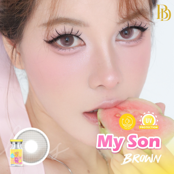 Close-up of a person with brown eyes holding an apple, featuring 'My Son Brown' contact lenses advertisement.