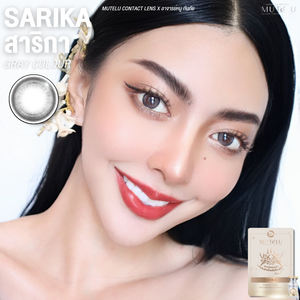 Woman with dark hair and red lipstick, wearing contact lenses, with Mute Lu  Sarika Gray contact lens packaging.