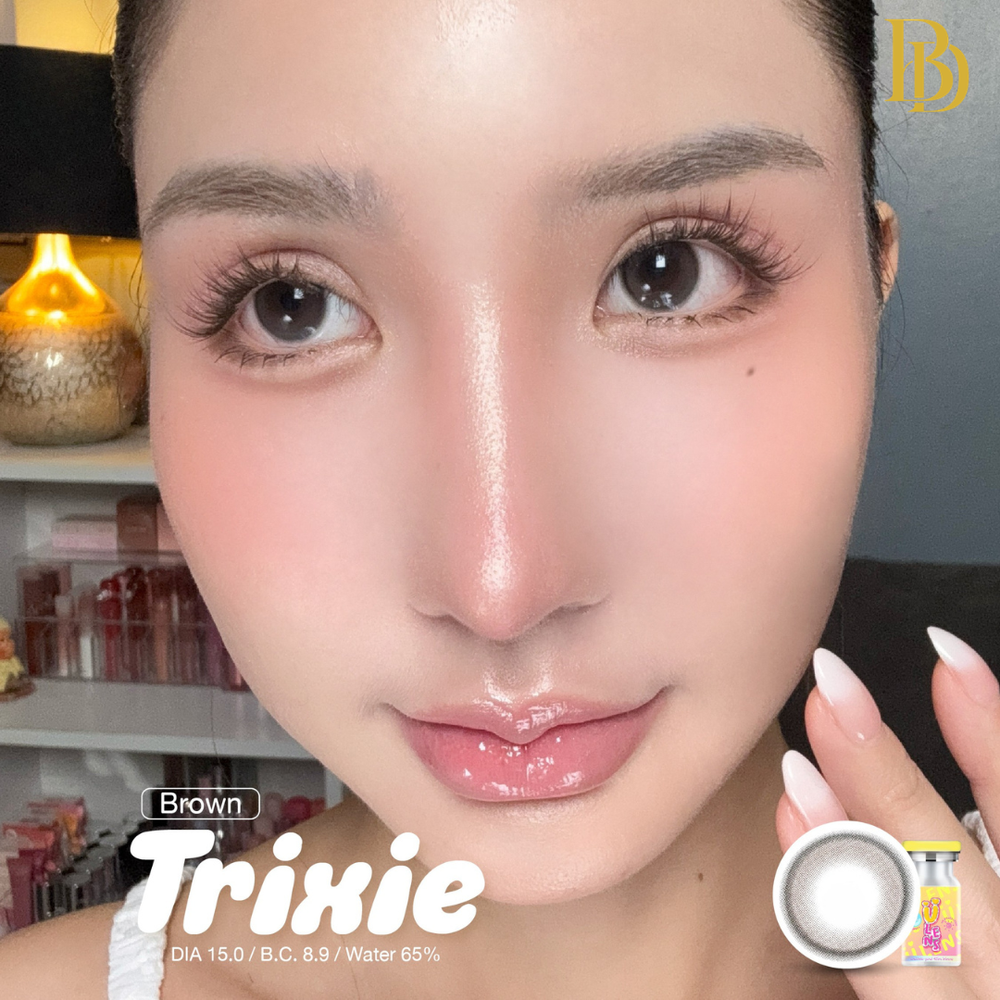 Close-up of a person holding a contact lens with 'Brown Trixie' branding.