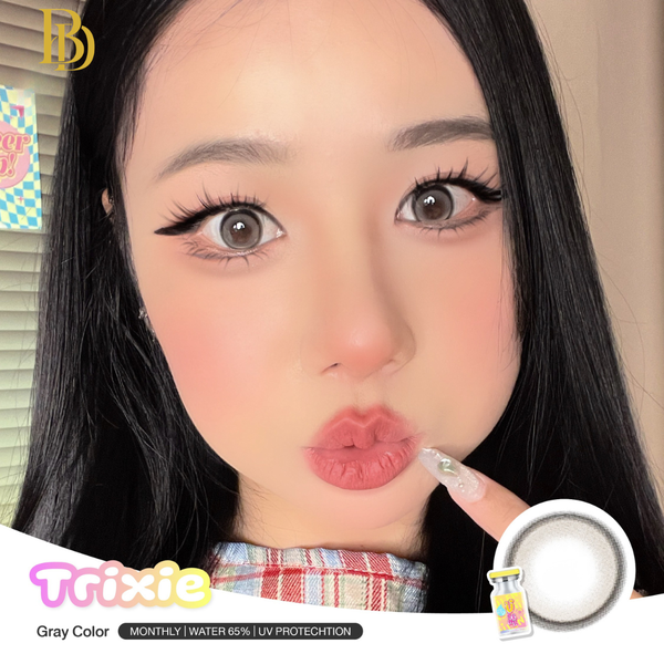 Close-up of a person with long dark hair and makeup, holding contact lenses with Trixie contact lenses branding.